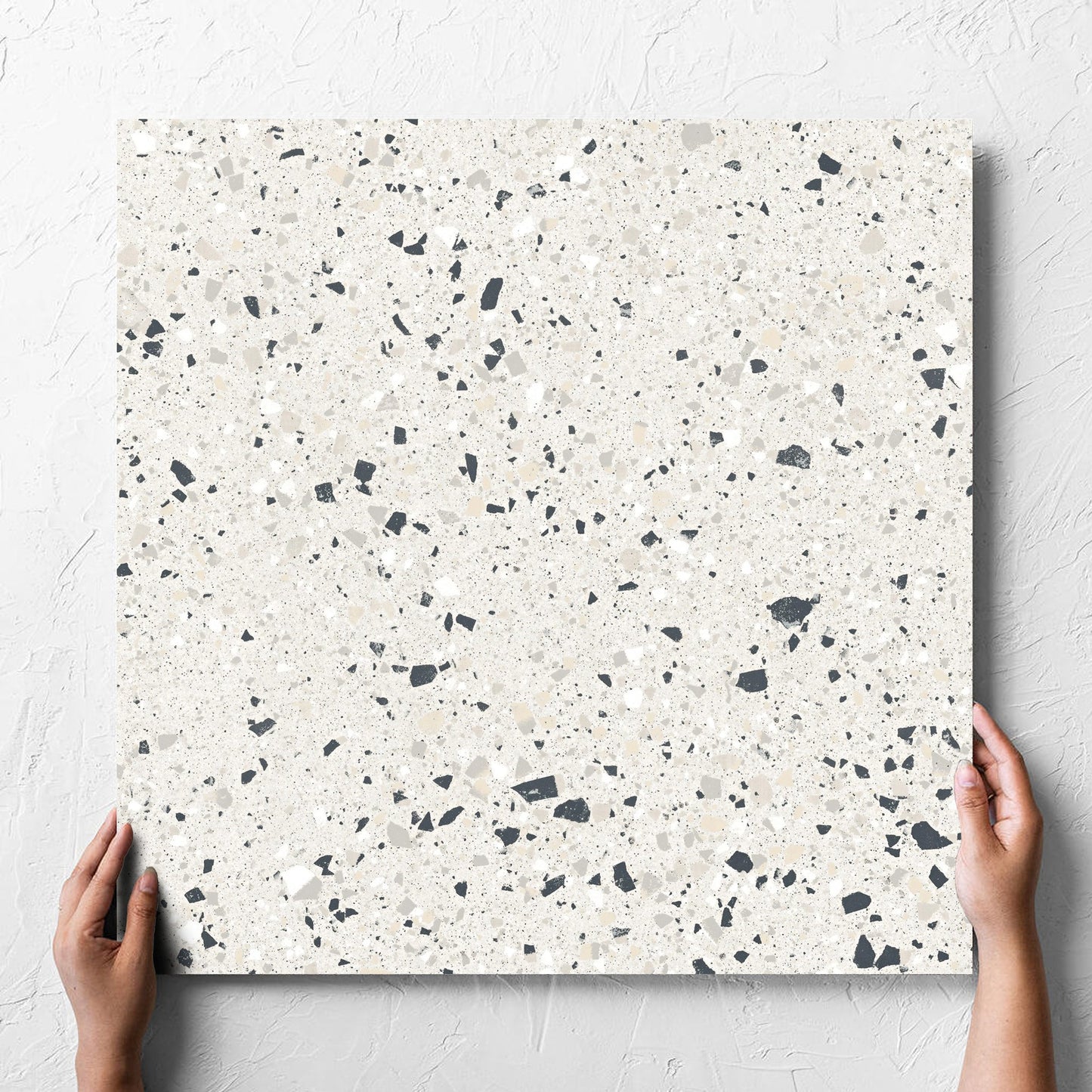 Hand holding a single C Venice 600x600 Matt Silver Terrazzo Look Rectified tile against a white rendered wall, showing the tile surface