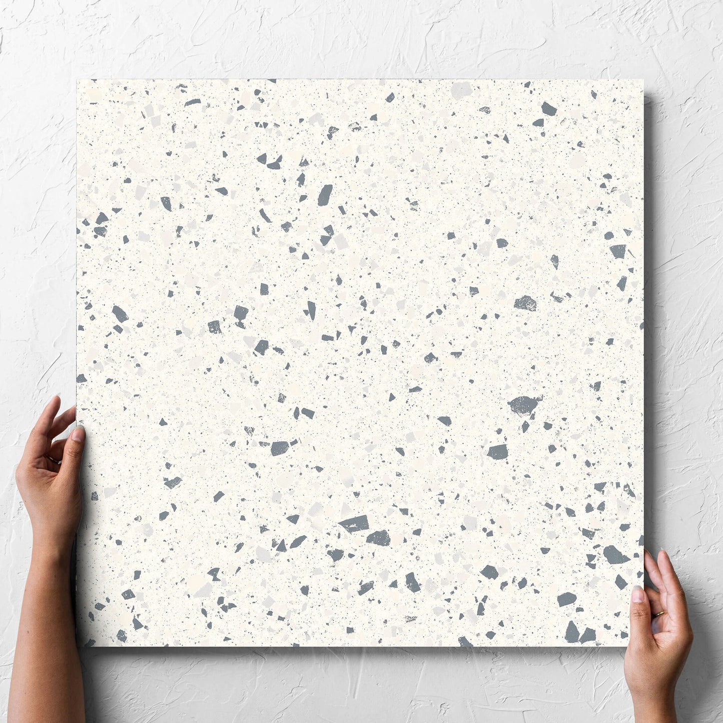 Hand holding a single C Venice 600x600 Matt White Terrazzo Look Rectified tile against a white rendered wall, showing the tile surface