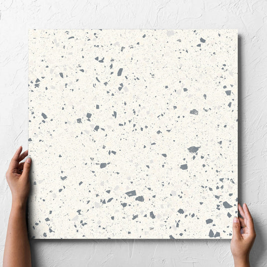 Hand holding a single C Venice 600x600 Matt White Terrazzo Look Rectified tile against a white rendered wall, showing the tile surface