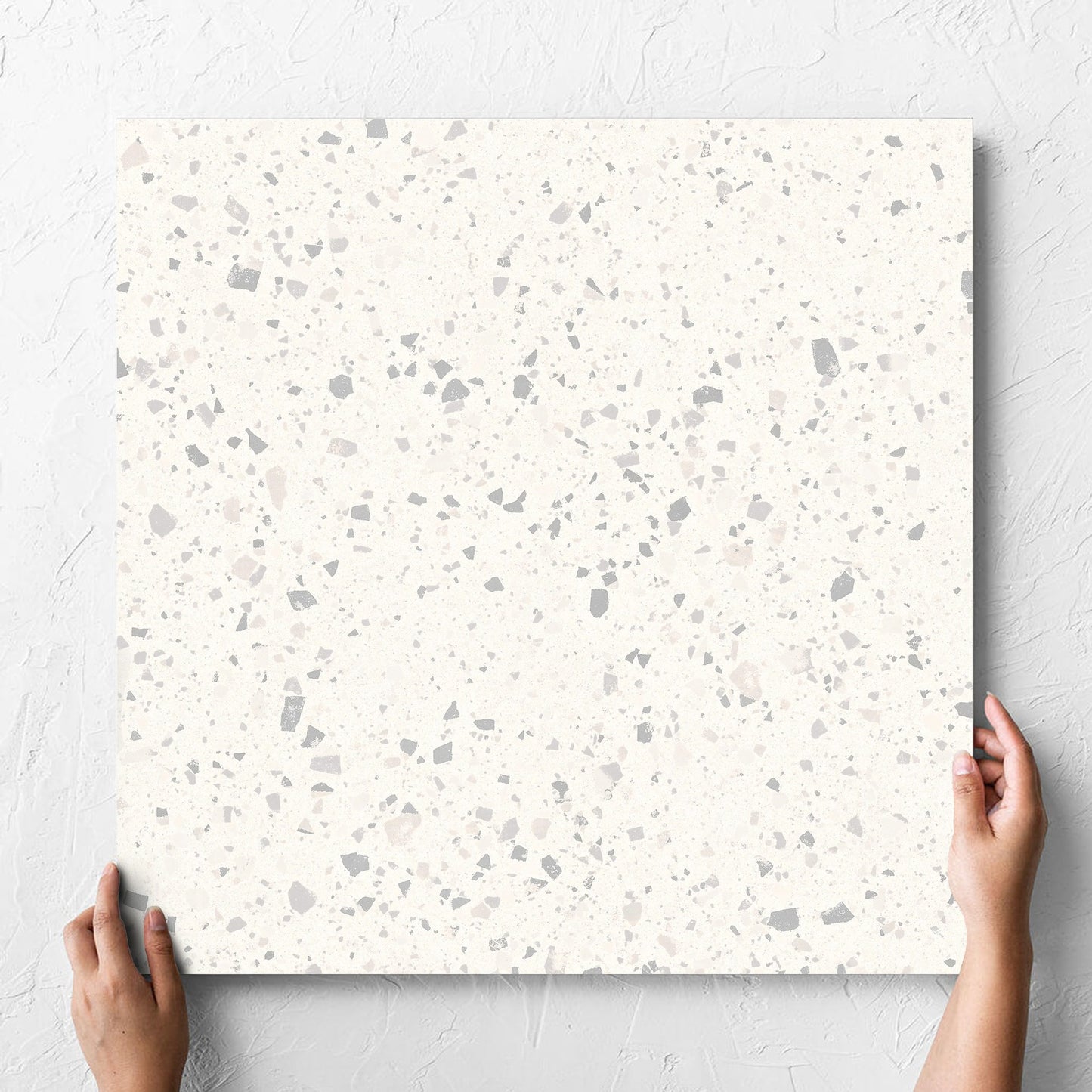 Hand holding a single C Venice 600x600 Matt Zinc Terrazzo Look Rectified tile against a white rendered wall, showing the tile surface