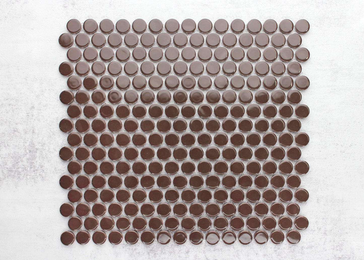 Flat lay pack shot of Cappuccino Gloss Diameter Glazed Porcelain Penny Round 19mm tiles showing glossy brown circular mosaic pieces arranged in a grid pattern on a white background.