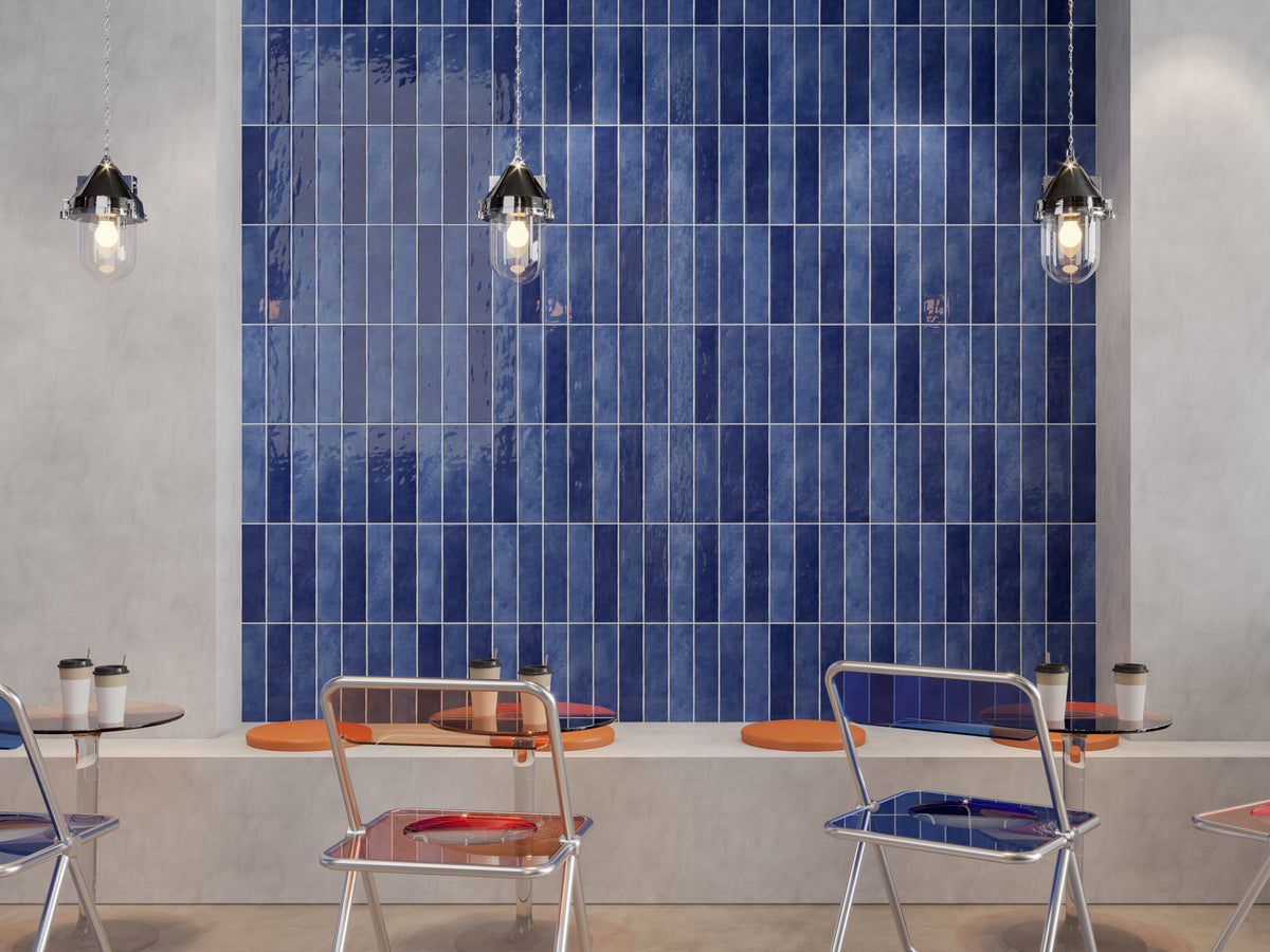 Caramela Dark Blue Gloss 75x300mm tiles laid vertically stacked on a cafe feature wall with pendant lights and orange seating.