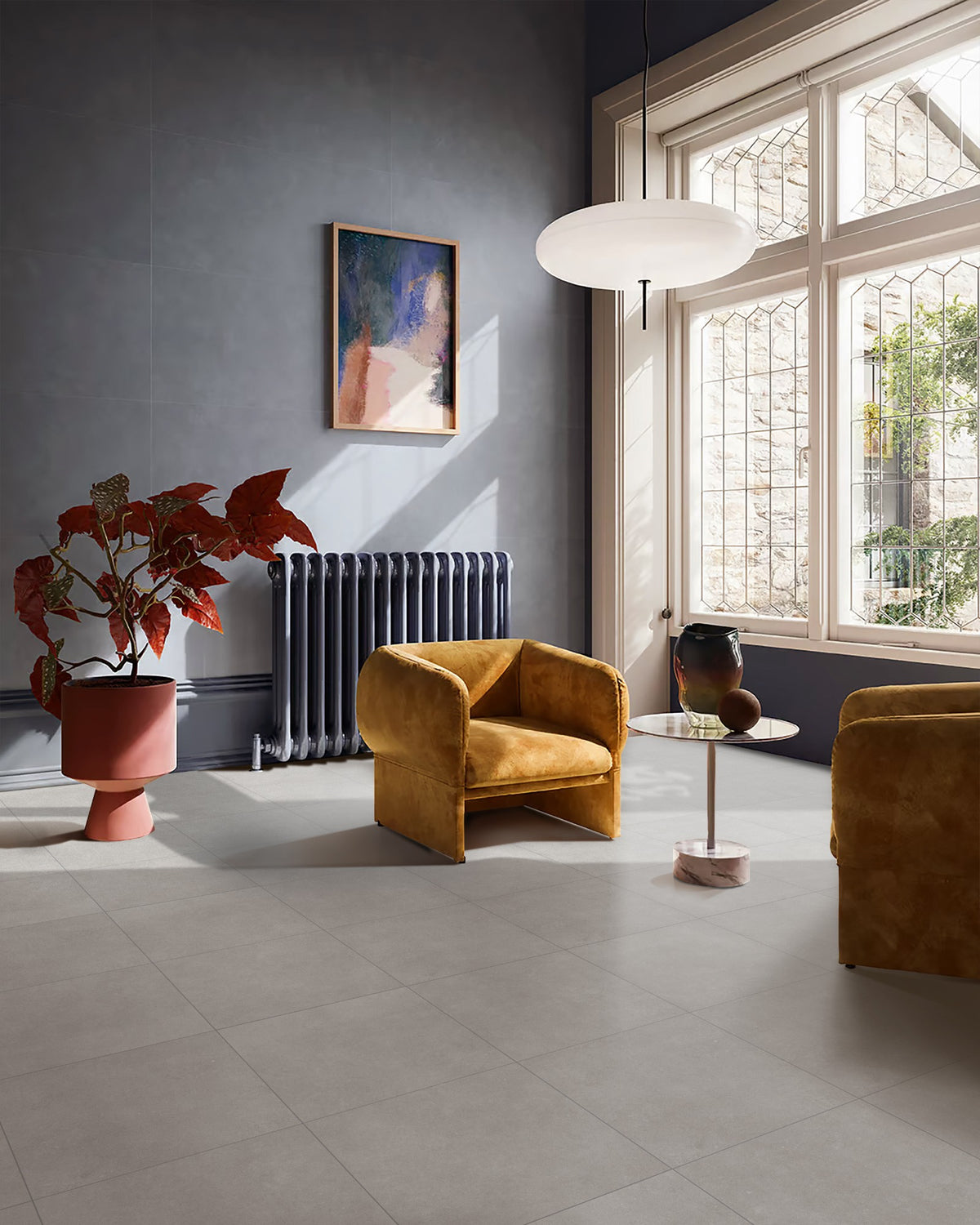 Carnarvon Grey Matt External 450x450mm tiles laid on a living room floor, styled with mustard velvet armchairs, a dark radiator, and a large leaded window.