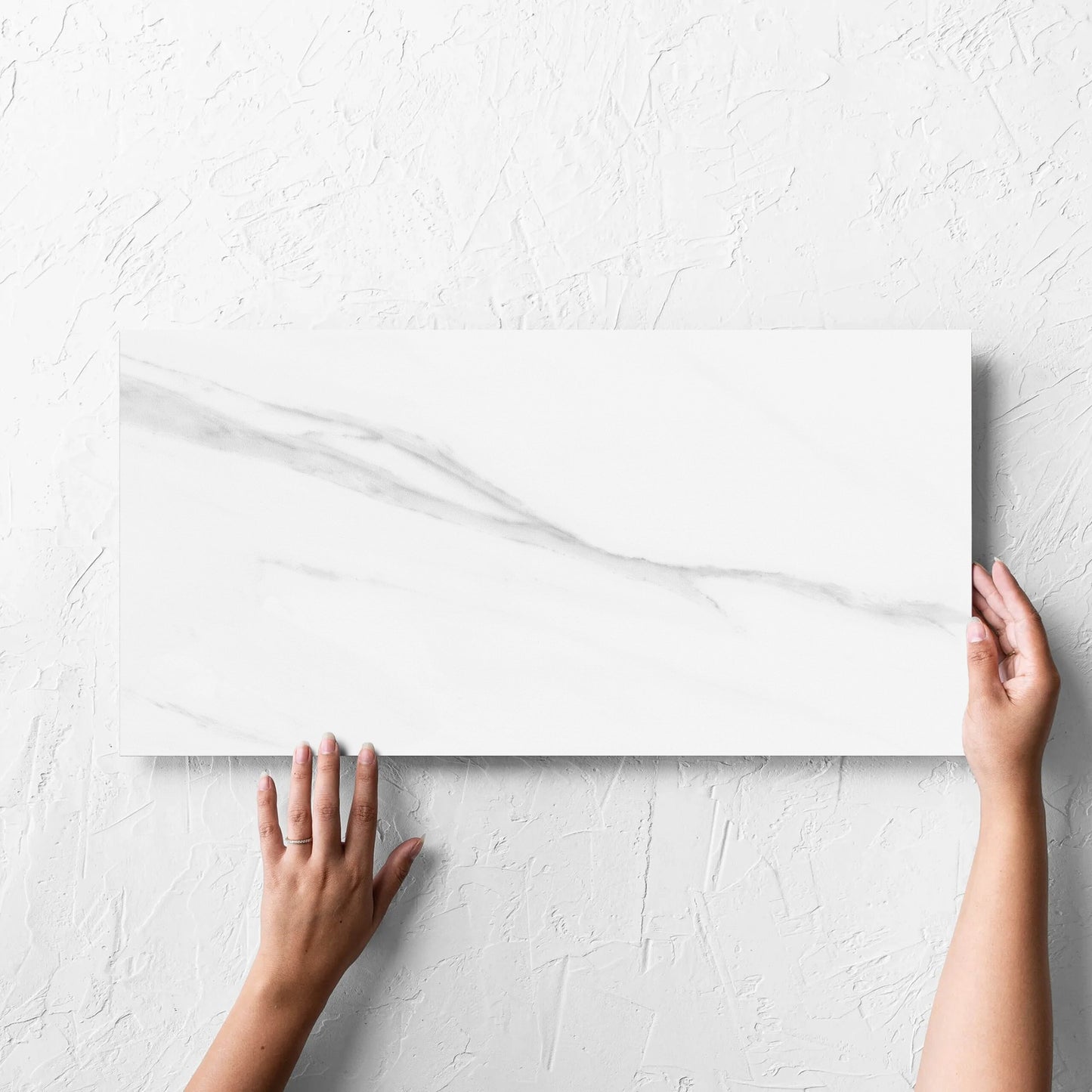 Hand holding a single Carrara Bianco Gloss 300x600mm tile against a white rendered wall, showing the gloss surface