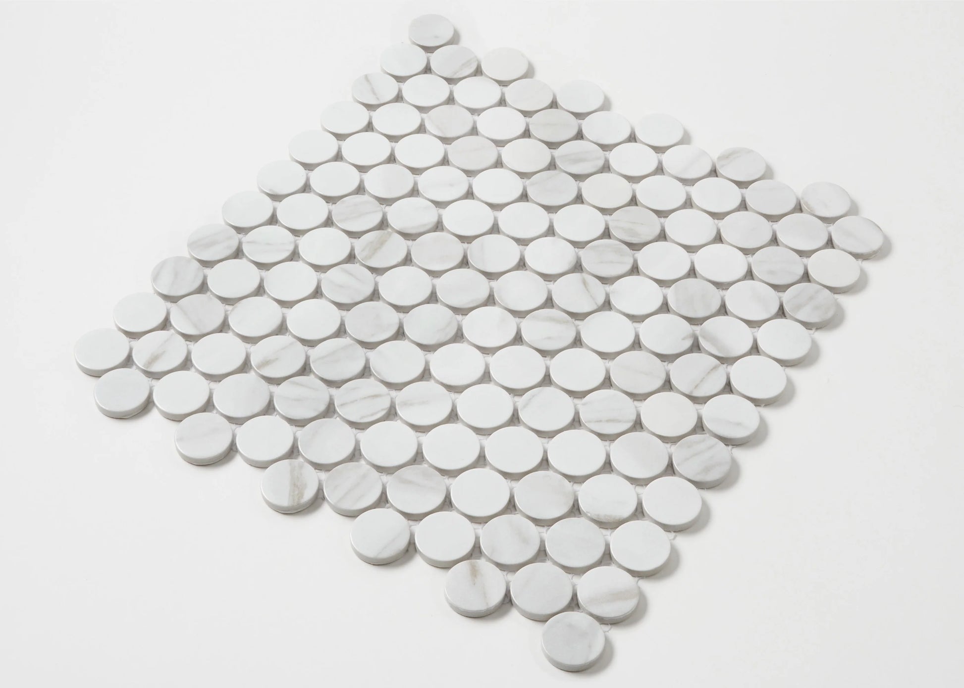 Pack shot of Carrara Look Matte Glazed Porcelain Penny Round 28mm Diameter tiles arranged in a diamond shape, showing white marble-effect circular discs with subtle grey veining.