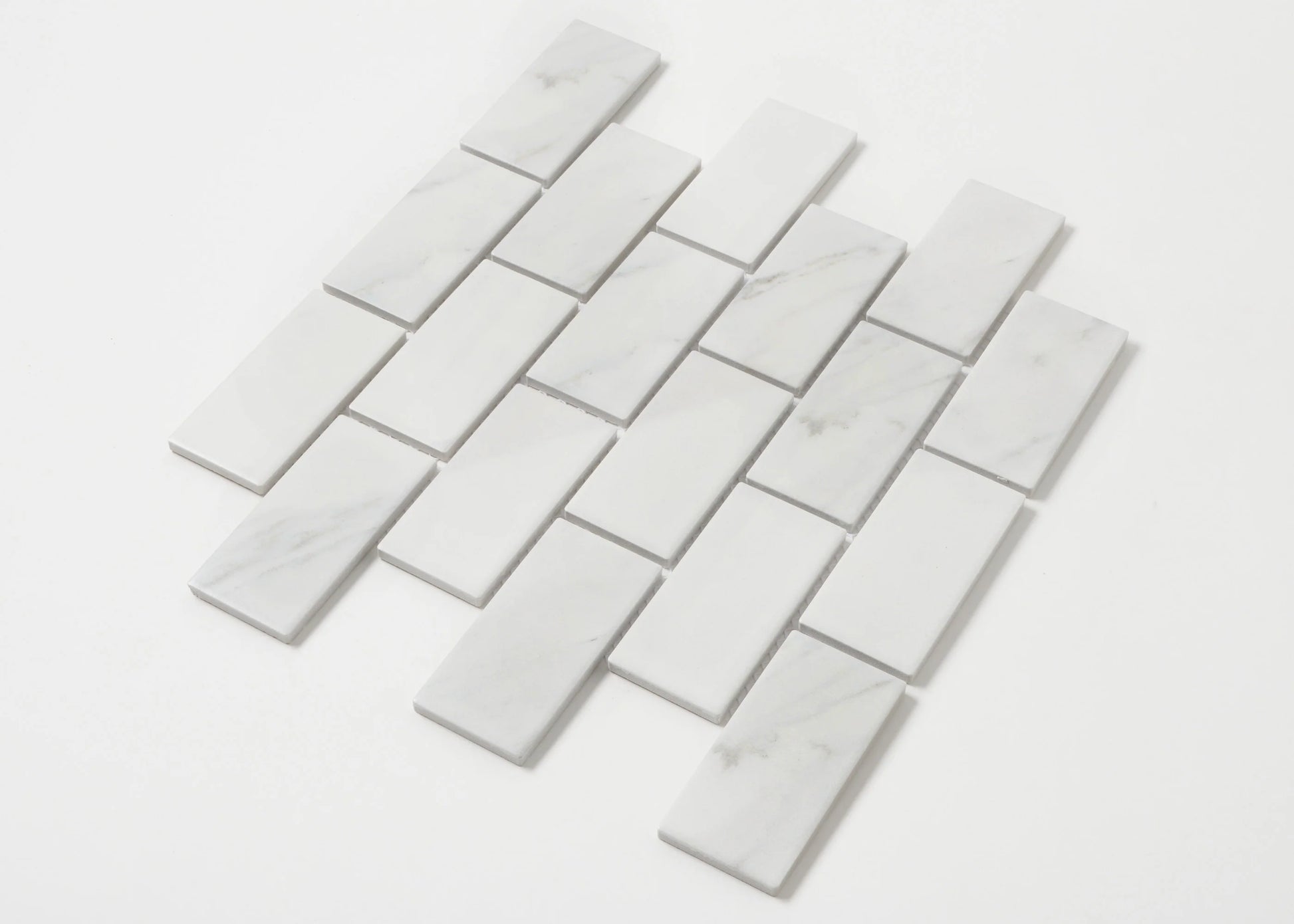 Pack shot of Carrara Look Matte Porcelain Glazed Brickbone 45x95mm tiles arranged in a staggered brick-bond layout, showing white marble-look finish with subtle grey veining.
