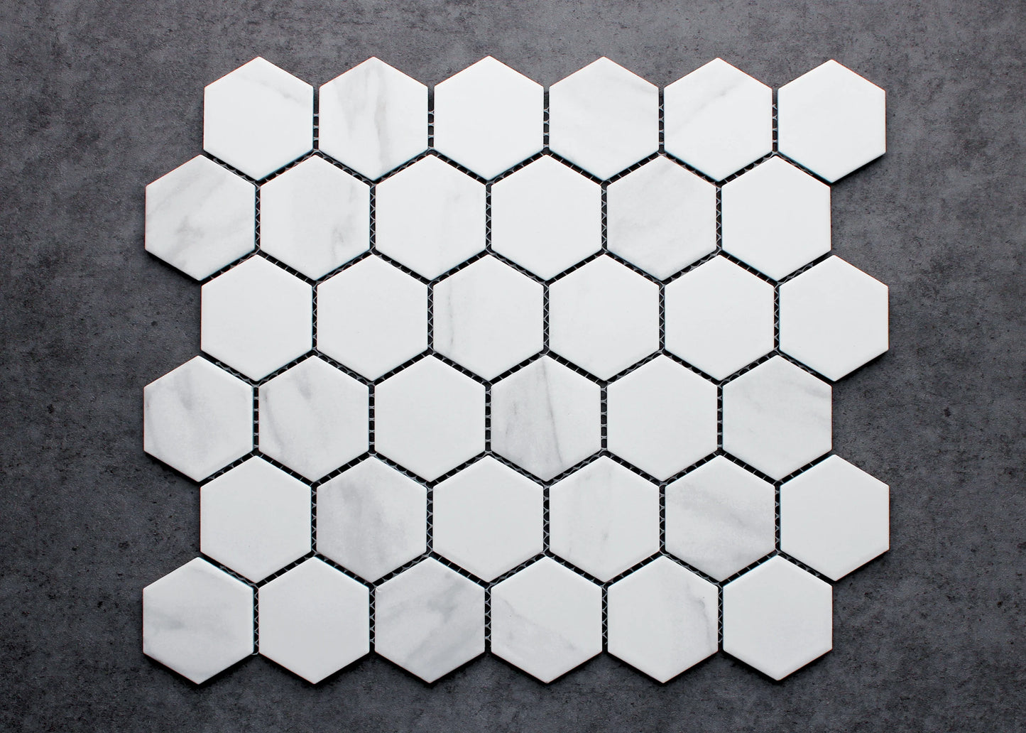 Flat lay pack shot of Carrara Look Matte Porcelain Glazed Hexagon 51x59mm tiles arranged in a honeycomb pattern, showing white matte finish with subtle grey veining.