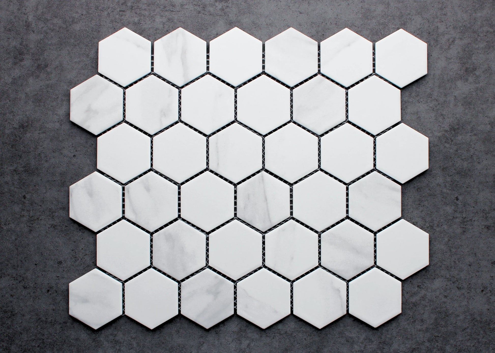 Flat lay pack shot of Carrara Look Matte Porcelain Glazed Hexagon 51x59mm tiles arranged in a honeycomb pattern, showing white matte finish with subtle grey veining.