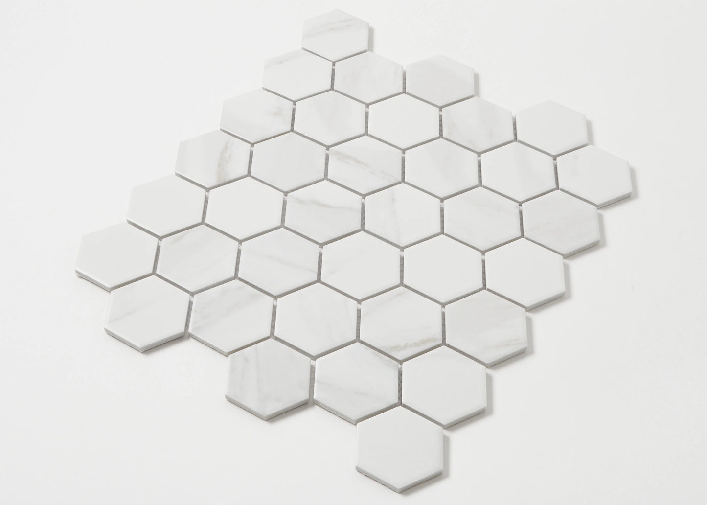 Pack shot of Carrara Look Matte Porcelain Glazed Hexagon 51x59mm tiles arranged in a honeycomb mosaic sheet, showing white matte finish with subtle grey marble veining.
