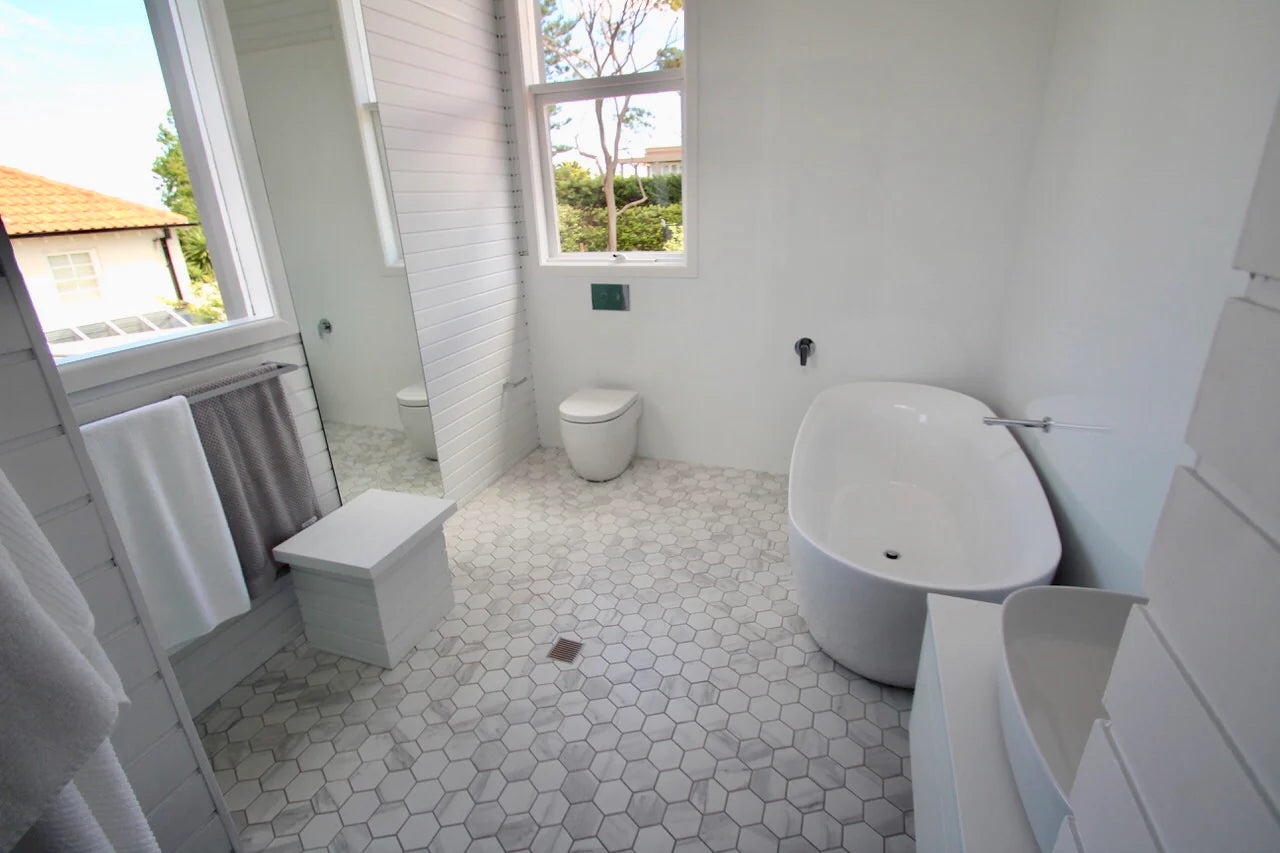 Carrara Matte Porcelain Glazed Hexagon 95x110mm tiles installed on a bright white bathroom floor beside a freestanding soaking tub and toilet.