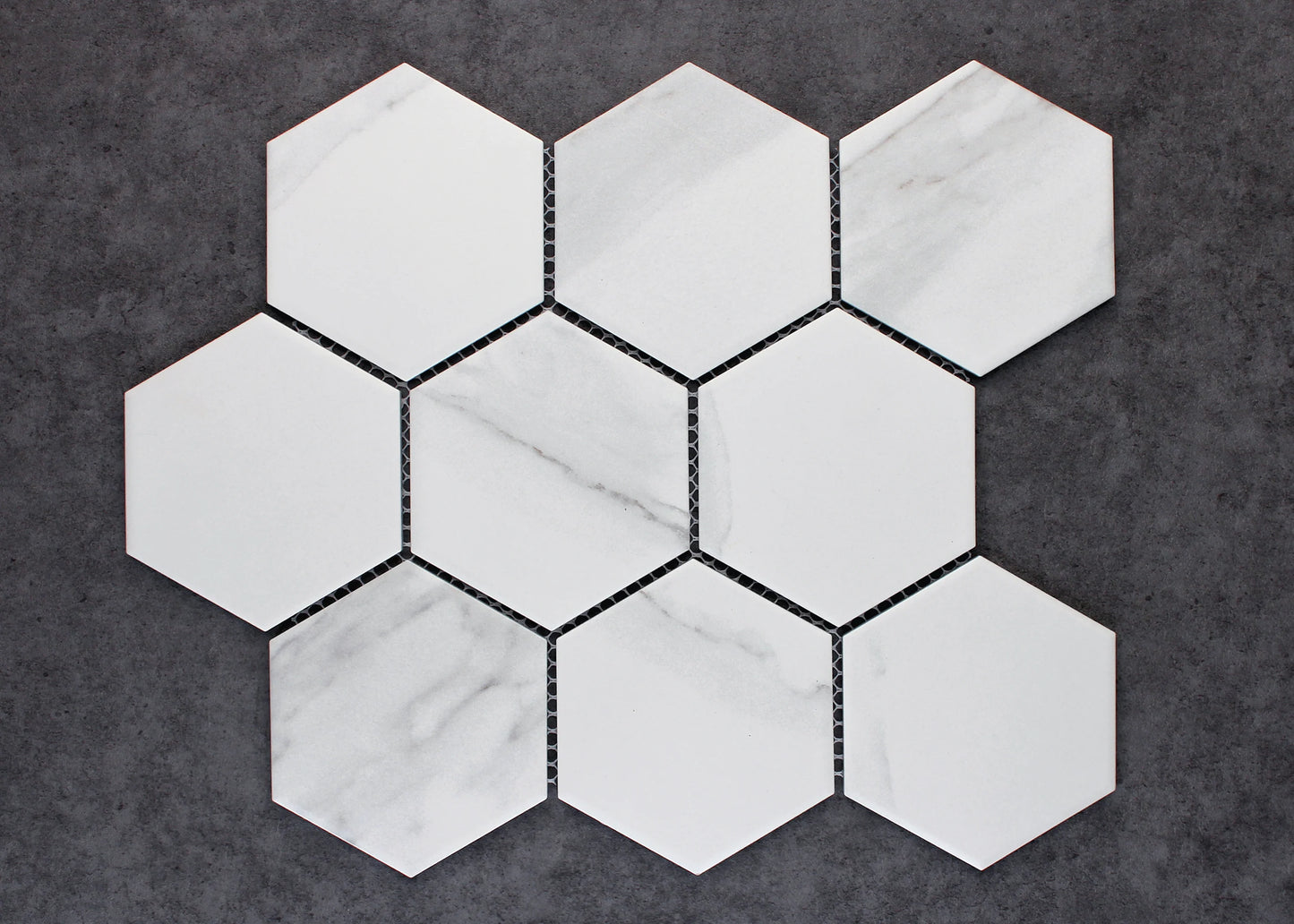 Nine Carrara Matte Porcelain Glazed Hexagon 95x110mm tiles arranged in a honeycomb cluster, showing white matte finish with subtle grey veining on a dark grey background.