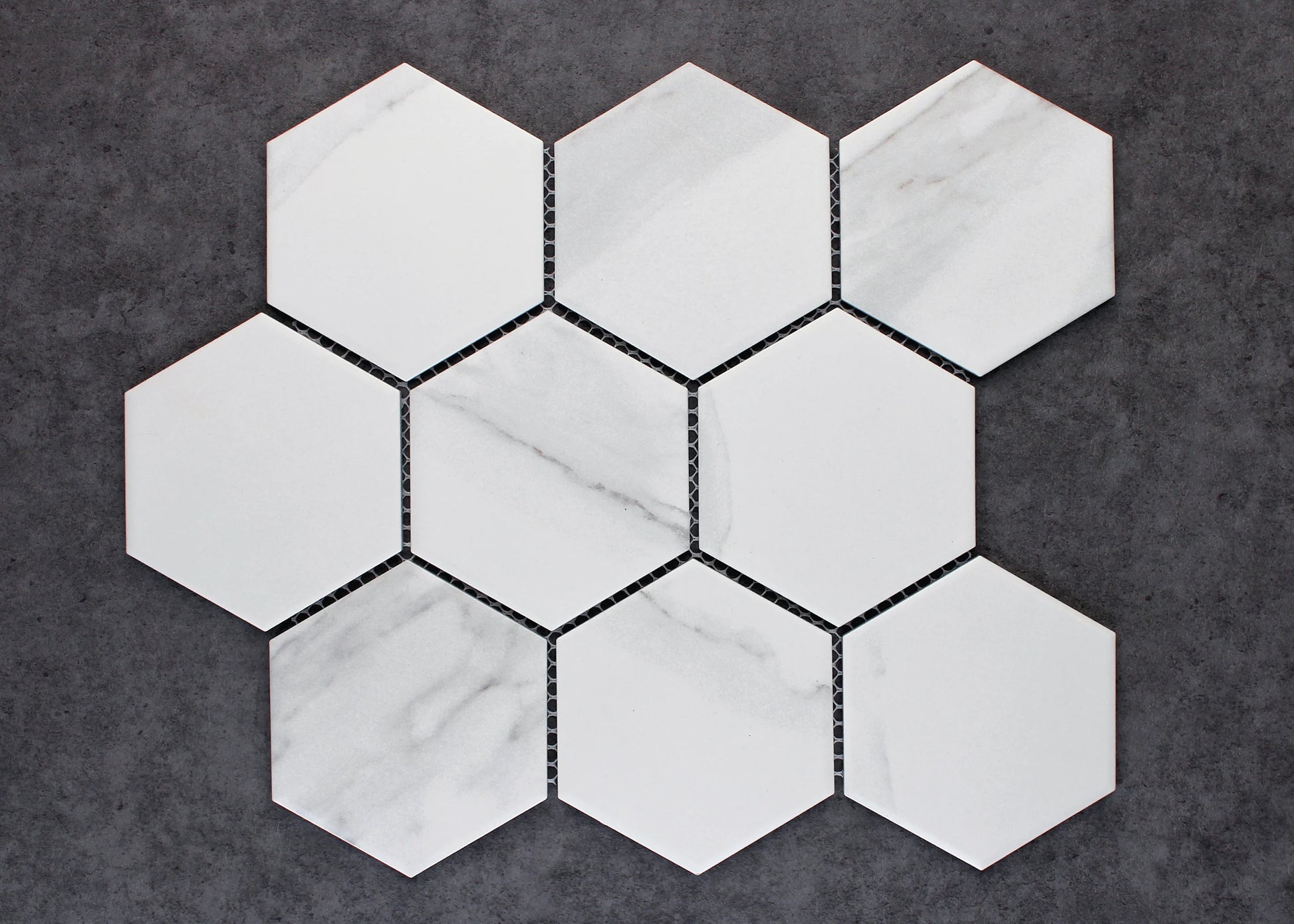 Nine Carrara Matte Porcelain Glazed Hexagon 95x110mm tiles arranged in a honeycomb cluster, showing white matte finish with subtle grey veining on a dark grey background.