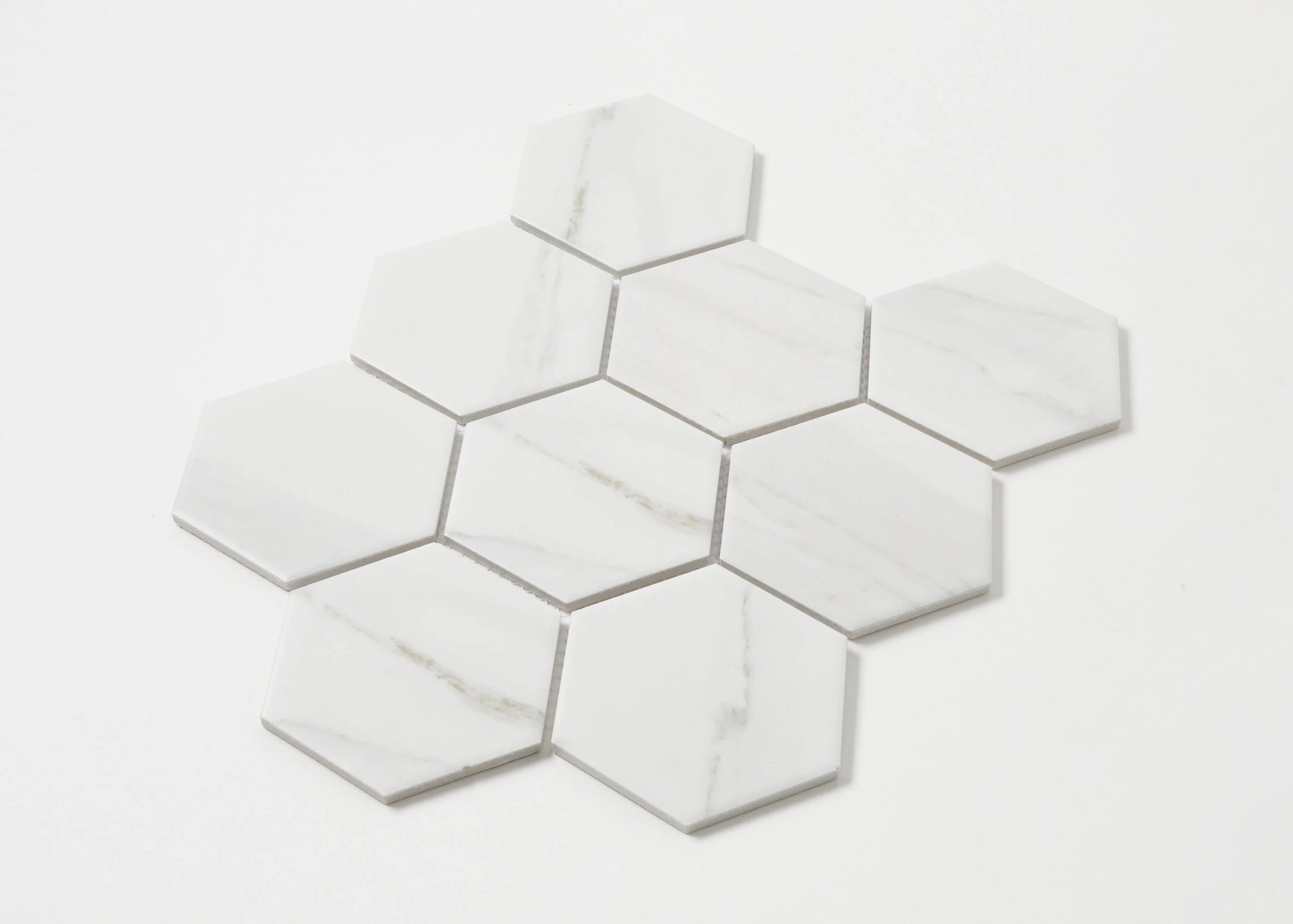 Pack shot of Carrara Matte Porcelain Glazed Hexagon 95x110mm tiles arranged in a cluster, showcasing white marble-look finish with subtle grey veining.