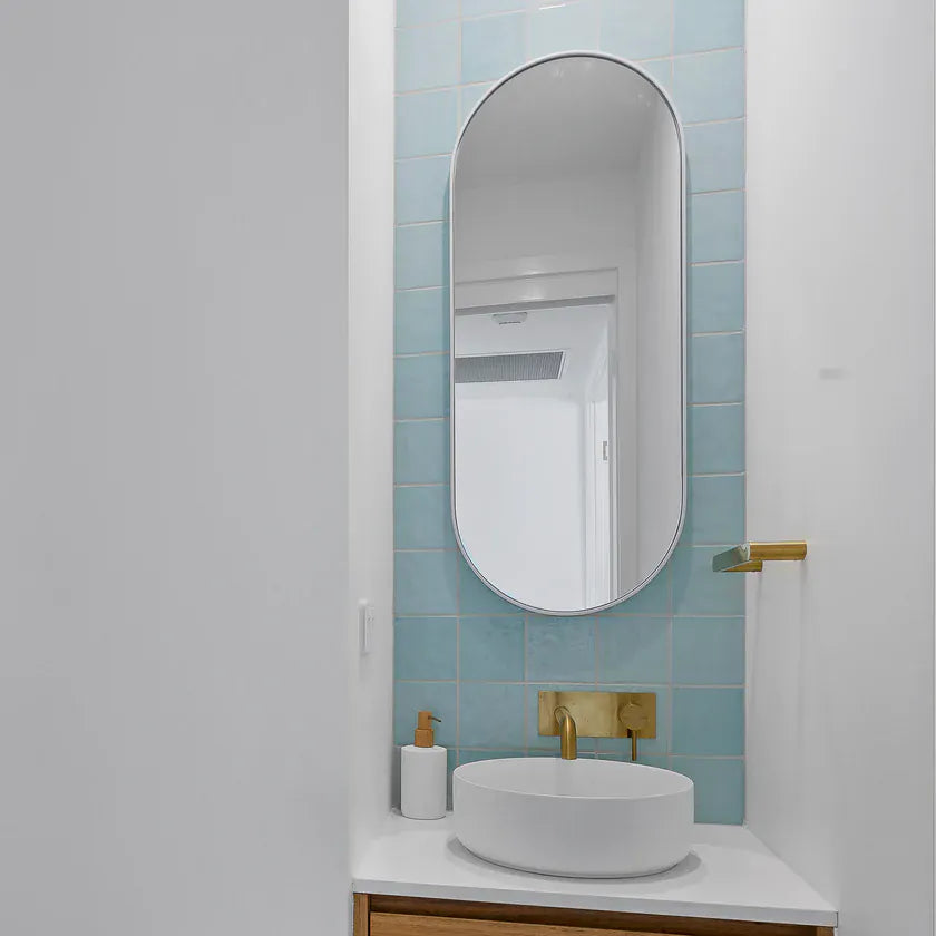 Casablanca Mint Gloss 120x120mm tiles form a soft aqua feature wall behind a round vessel sink with brushed brass tapware and an oval mirror.