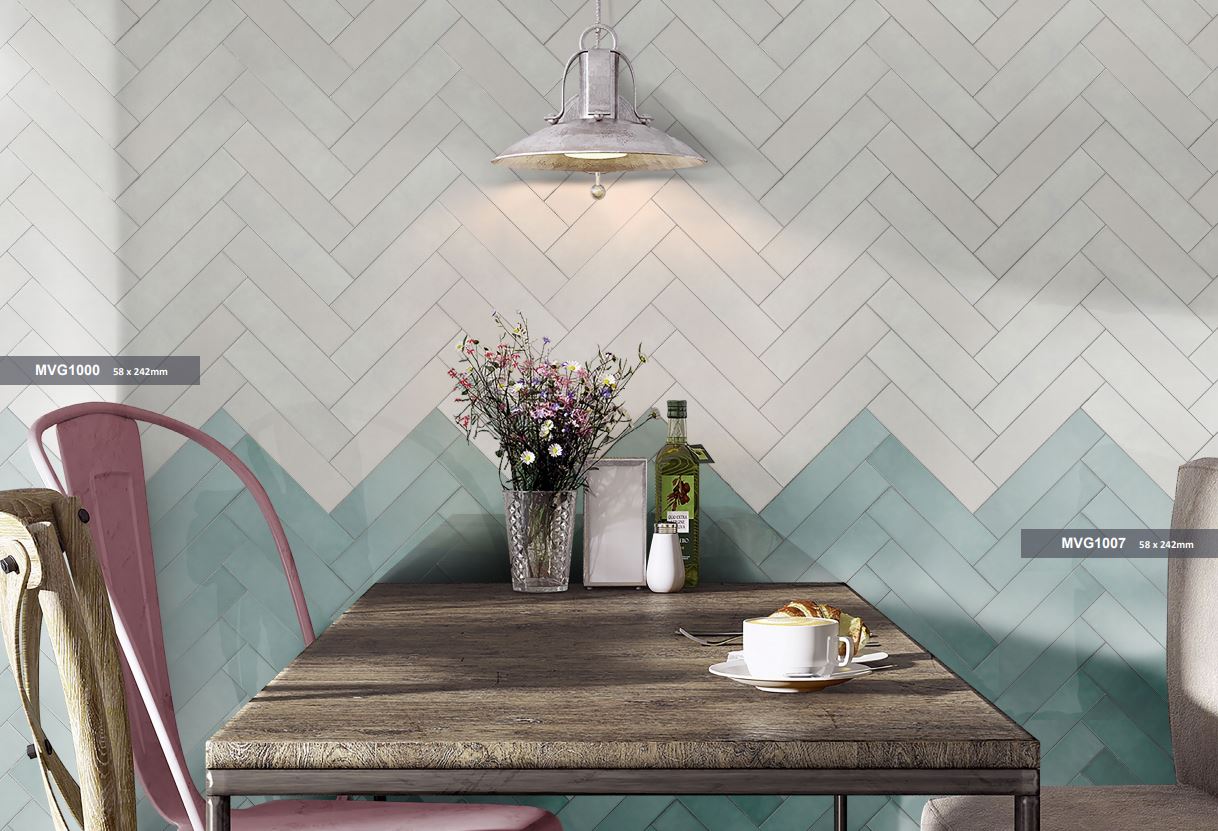 Casablanca Mint Gloss 58x242mm tiles installed in a chevron herringbone pattern on a café wall, paired with white tiles, a rustic timber table, and an industrial pendant light.