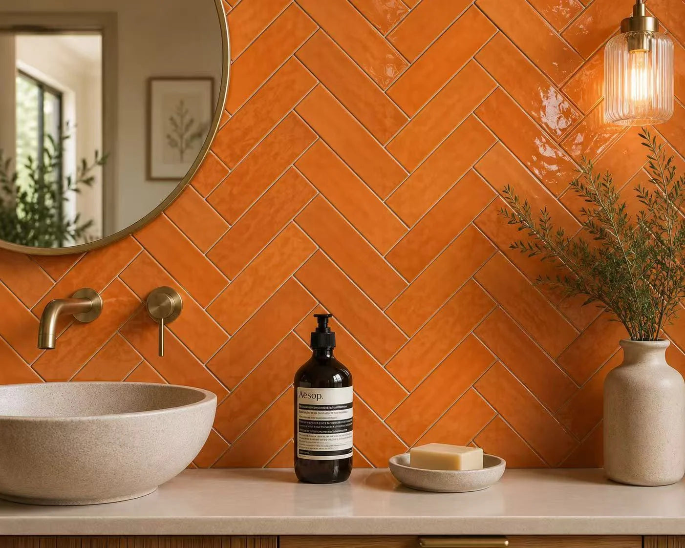 Casablanca Orange Gloss 58x242mm tiles laid in a herringbone pattern on a bathroom vanity wall, paired with brass fixtures, a round mirror, and a ribbed pendant light.