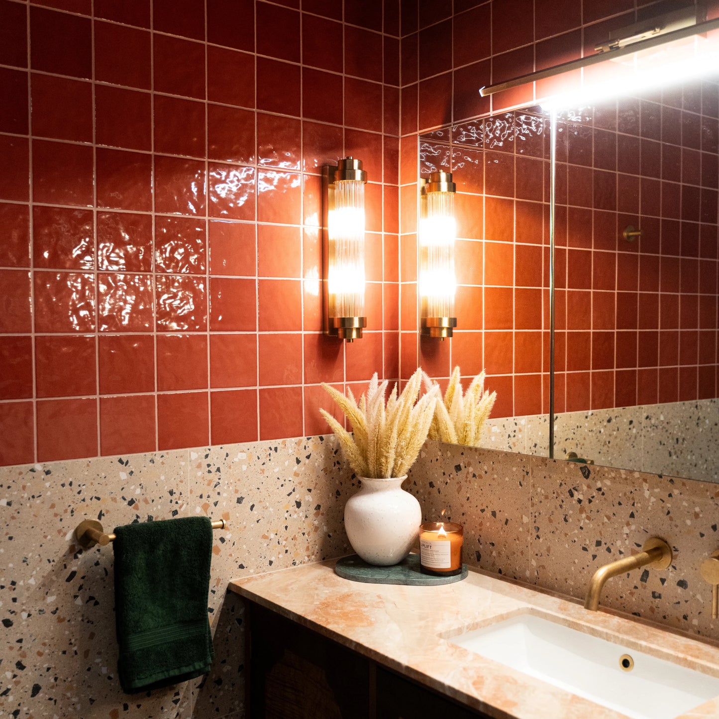 Casablanca Red Gloss 120x120mm tiles covering a bathroom wall above terrazzo dado, paired with brass wall sconces, a marble vanity, and decorative dried grasses.