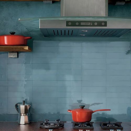 Casablanca Sky Blue Gloss 58x242mm tiles installed as a kitchen splashback behind a stainless steel range hood with red cast iron cookware on open shelving and stovetop.