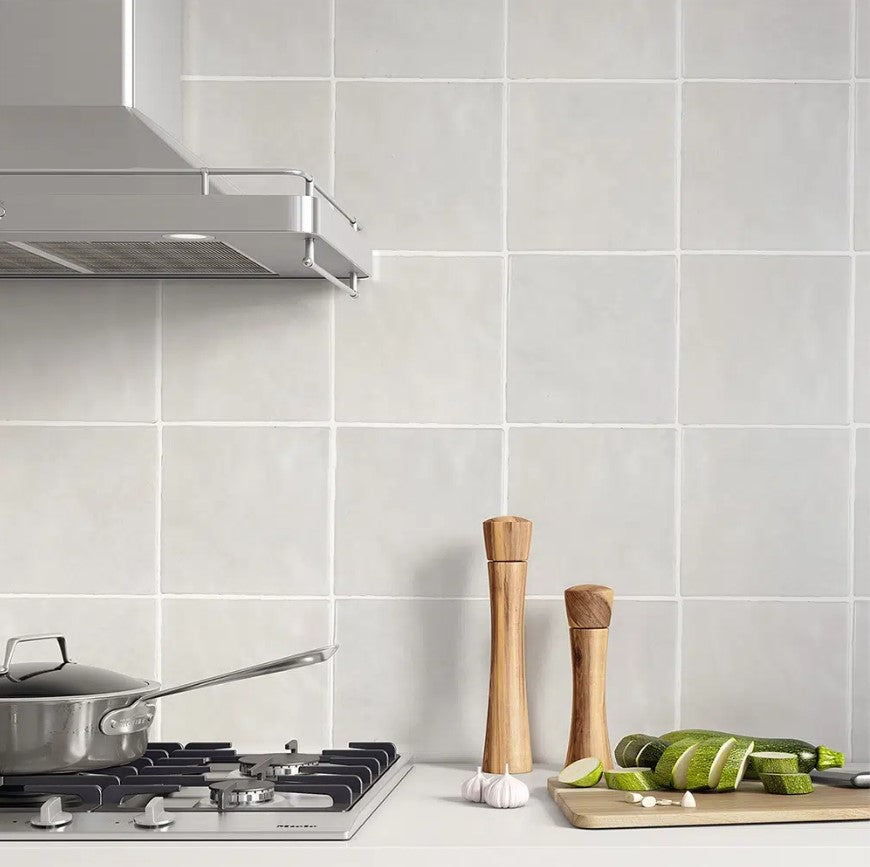 Casablanca White Matte 120x120mm tiles installed as a kitchen splashback behind a gas hob, range hood, and wooden pepper grinders with sliced zucchini on a chopping board.