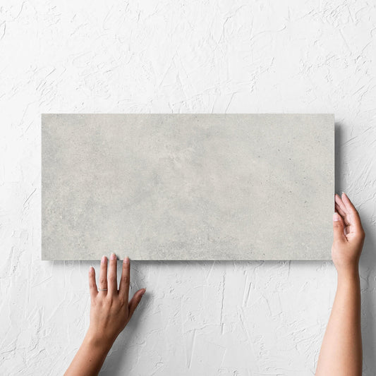 Hand holding a single Cement Dark Grey Matt 300x600mm tile against a white rendered wall, showing the matt surface