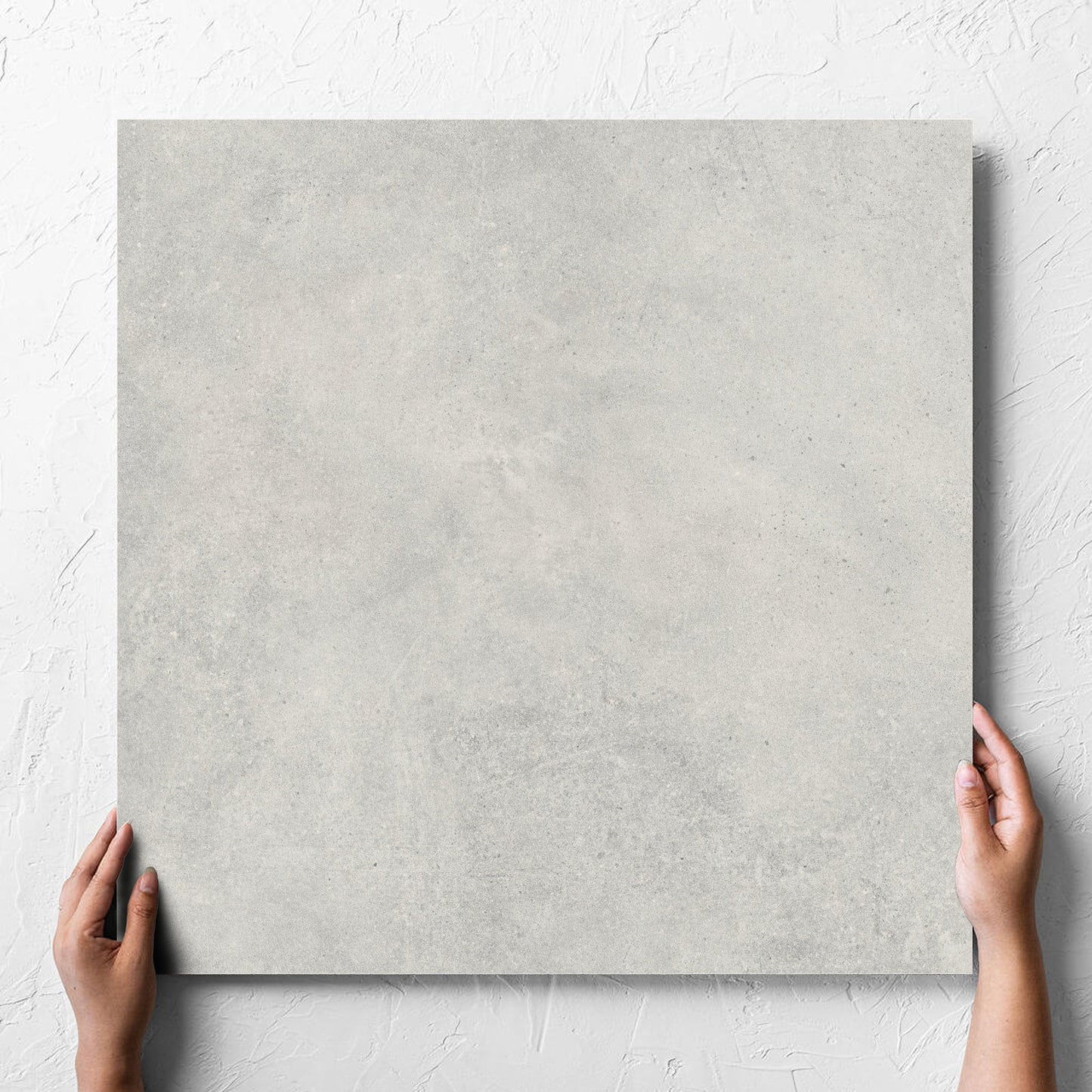 Hand holding a single Cement Dark Grey Matt 600x600mm tile against a white rendered wall, showing the matt surface