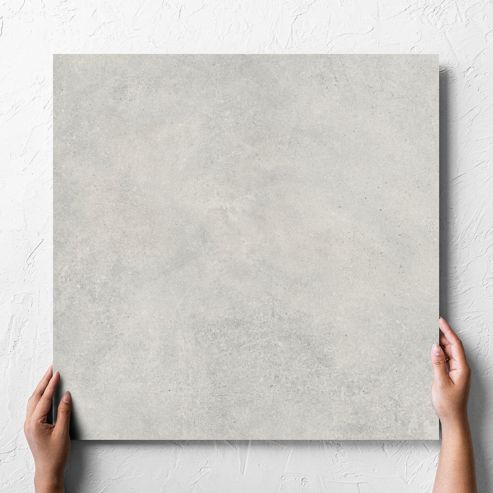 Hand holding a single Cement Dark Grey Matt 600x600mm tile against a white rendered wall, showing the matt surface