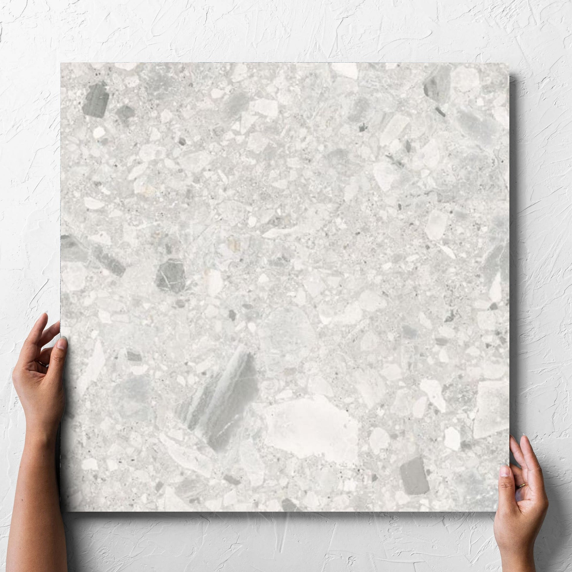 Hand holding a single Ceppo Bianco External 600x600mm tile against a white rendered wall, showing the bianco matt surface