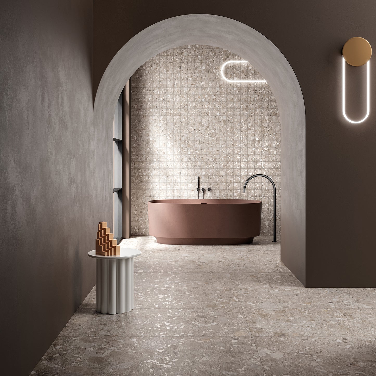 Ceppo Dark Beige InOut 600x600mm terrazzo-effect tiles covering the floor and mosaic feature wall of a luxurious arched bathroom with a freestanding terracotta bathtub and sculptural wall light.