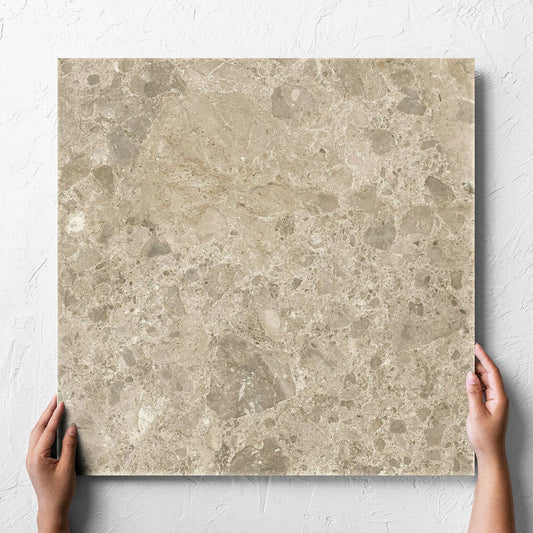 Hand holding a single Ceppo Dark Beige InOut 600x600mm tile against a white rendered wall, showing the tile surface