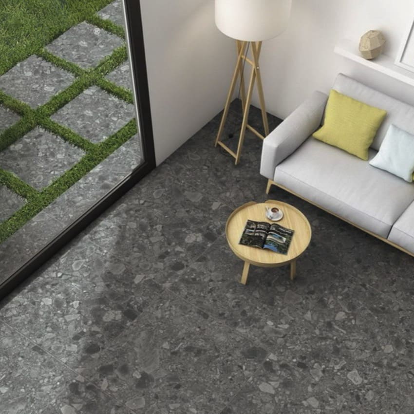 Ceppo Grey InOut 300x600mm dark terrazzo-effect tiles installed on a modern living room floor with sofa, floor lamp, and outdoor patio view.