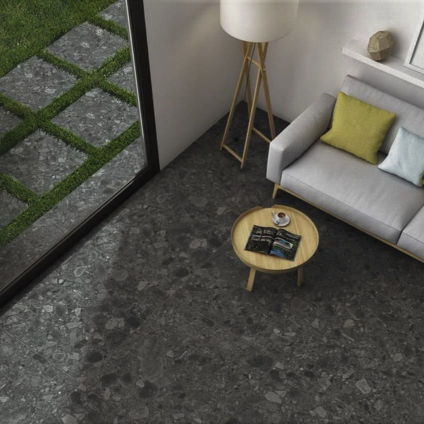 Ceppo Nero InOut 600x600mm dark terrazzo-effect tiles installed across a modern living room floor, styled with a grey sofa, timber coffee table, and floor lamp.