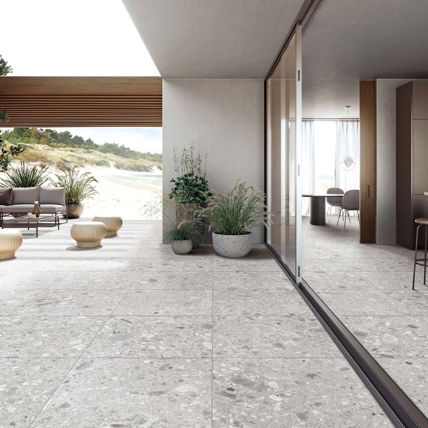 Ceppo Stone InOut 600x600mm light grey terrazzo-effect tiles installed seamlessly across an open coastal terrace and modern indoor dining space with glass sliding doors and potted plants.