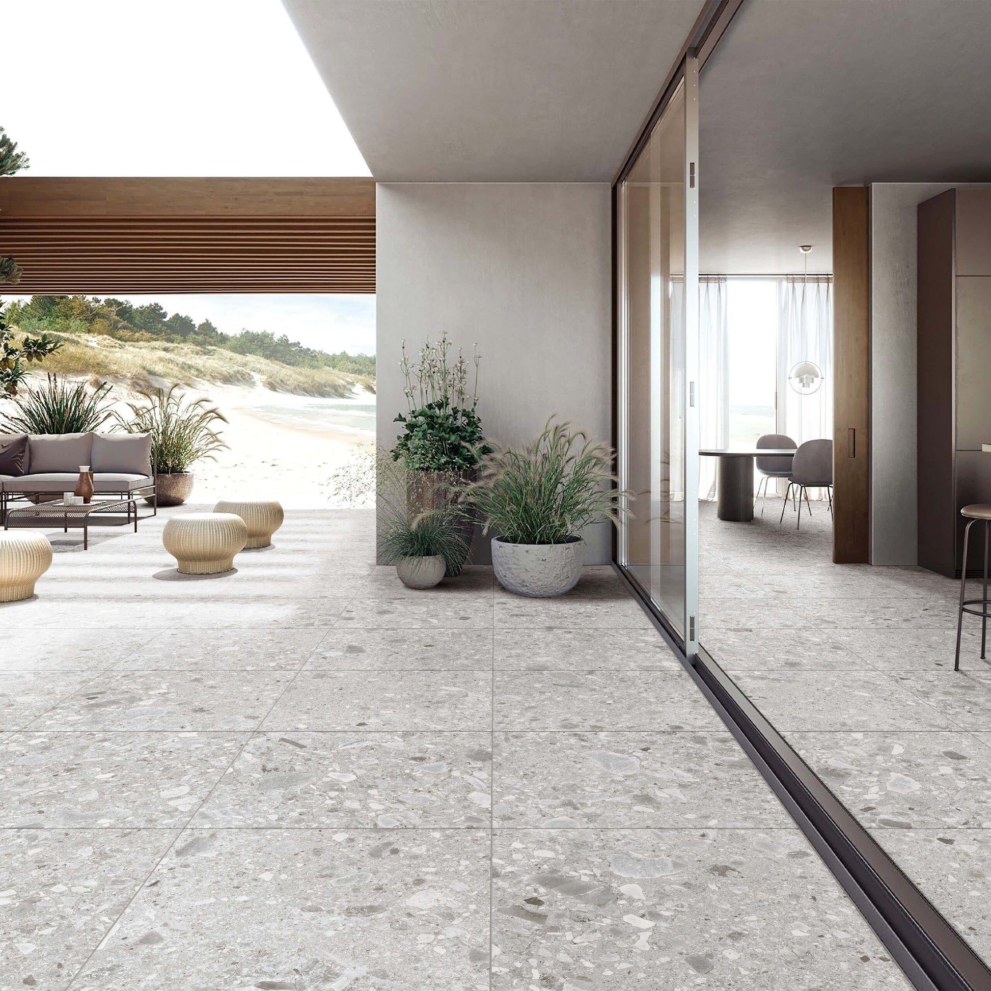 Ceppo Stone InOut 600x600mm light grey terrazzo-effect tiles installed seamlessly across an open coastal terrace and modern indoor dining space with glass sliding doors and potted plants.
