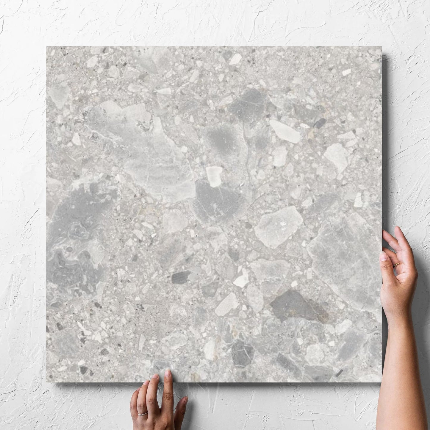 Hand holding a single Ceppo Stone InOut 600x600mm tile against a white rendered wall, showing the tile surface