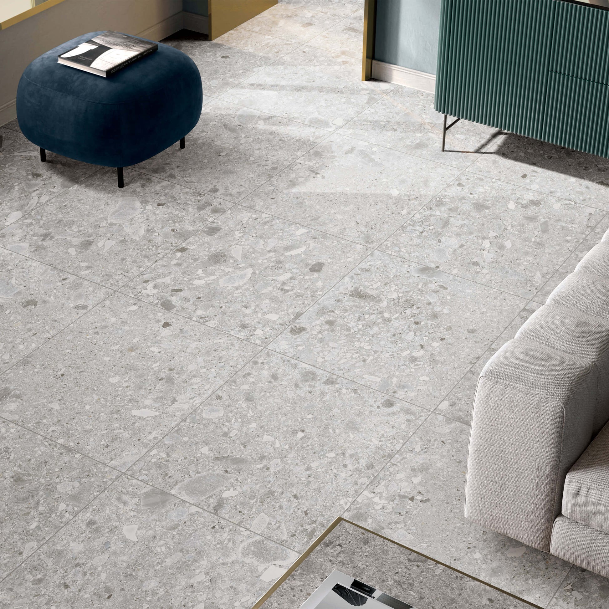 Ceppo Stone InOut 600x600mm light grey terrazzo-effect floor tiles installed in a modern living room with a blue velvet ottoman and cream sofa.