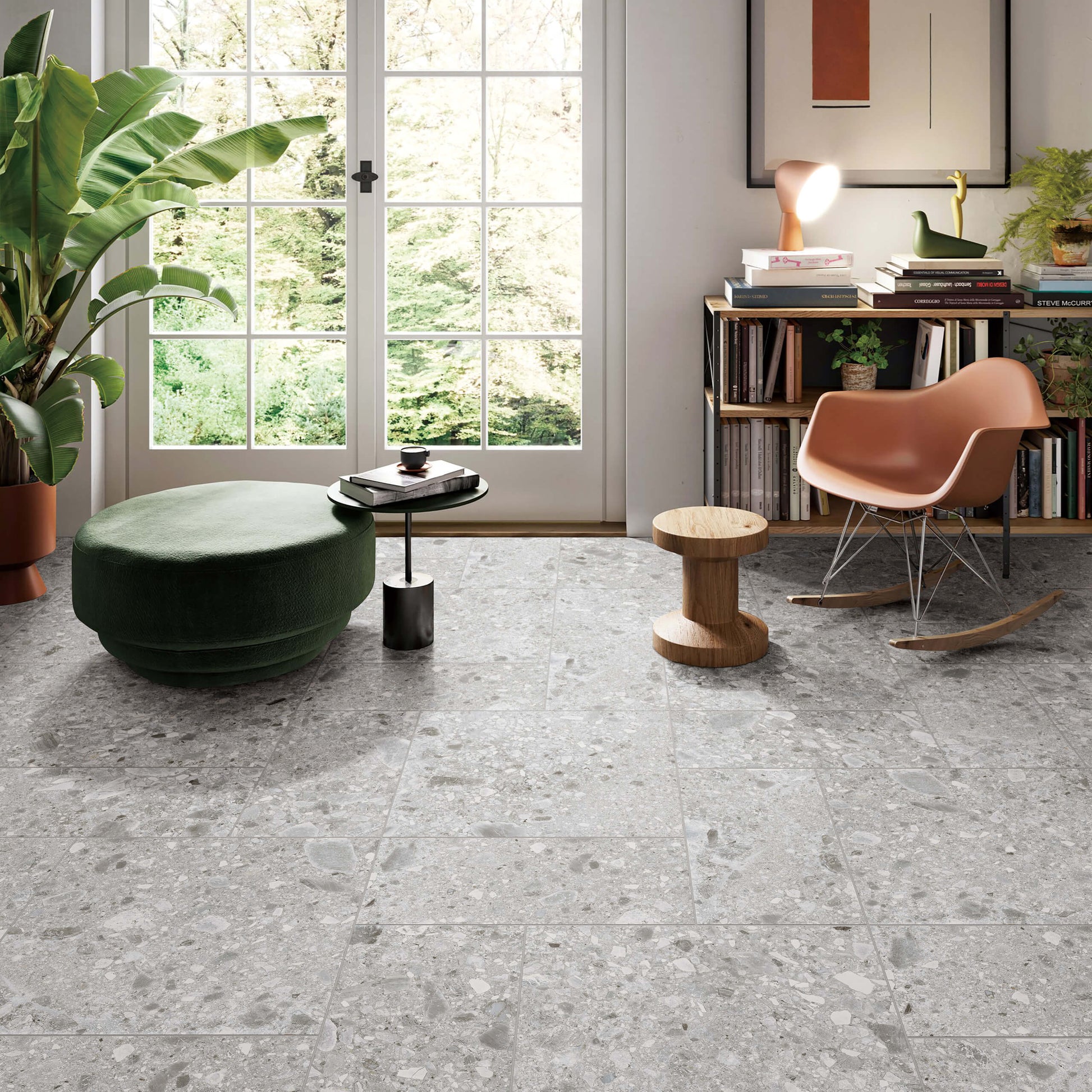 Ceppo Stone InOut 600x600mm grey terrazzo-effect floor tiles installed in a bright living room with a green ottoman, rocking chair, and large French doors.