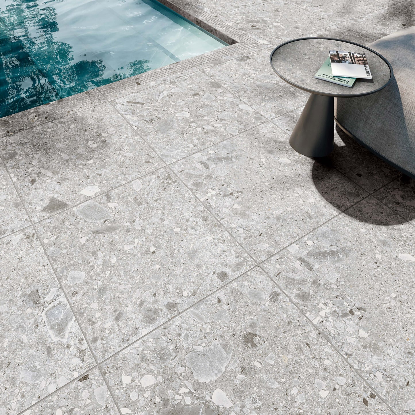 Ceppo Stone InOut 600x600mm light grey terrazzo-look tiles installed on a poolside patio with a modern side table and magazine.