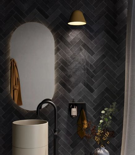 Chroma Black Gloss 52x160mm tiles laid in a herringbone pattern on a dramatic bathroom feature wall behind a cylindrical pedestal vanity and pendant light.