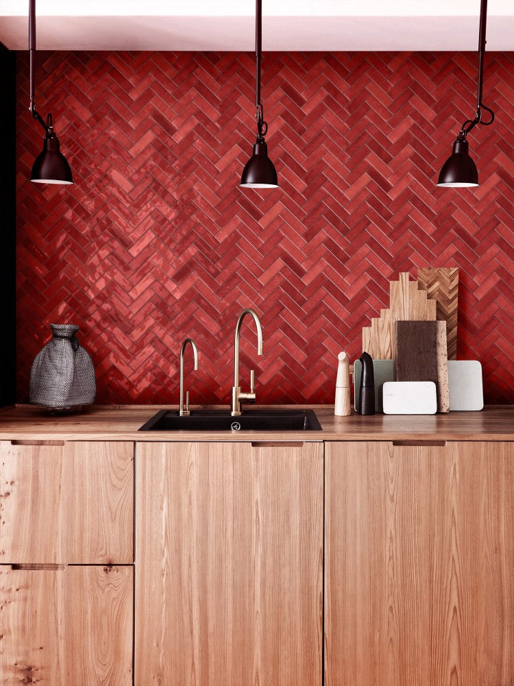 Chroma Rosso Matt 52x160mm tiles installed in a herringbone pattern kitchen splashback behind a black sink with brass faucet and natural wood cabinetry.