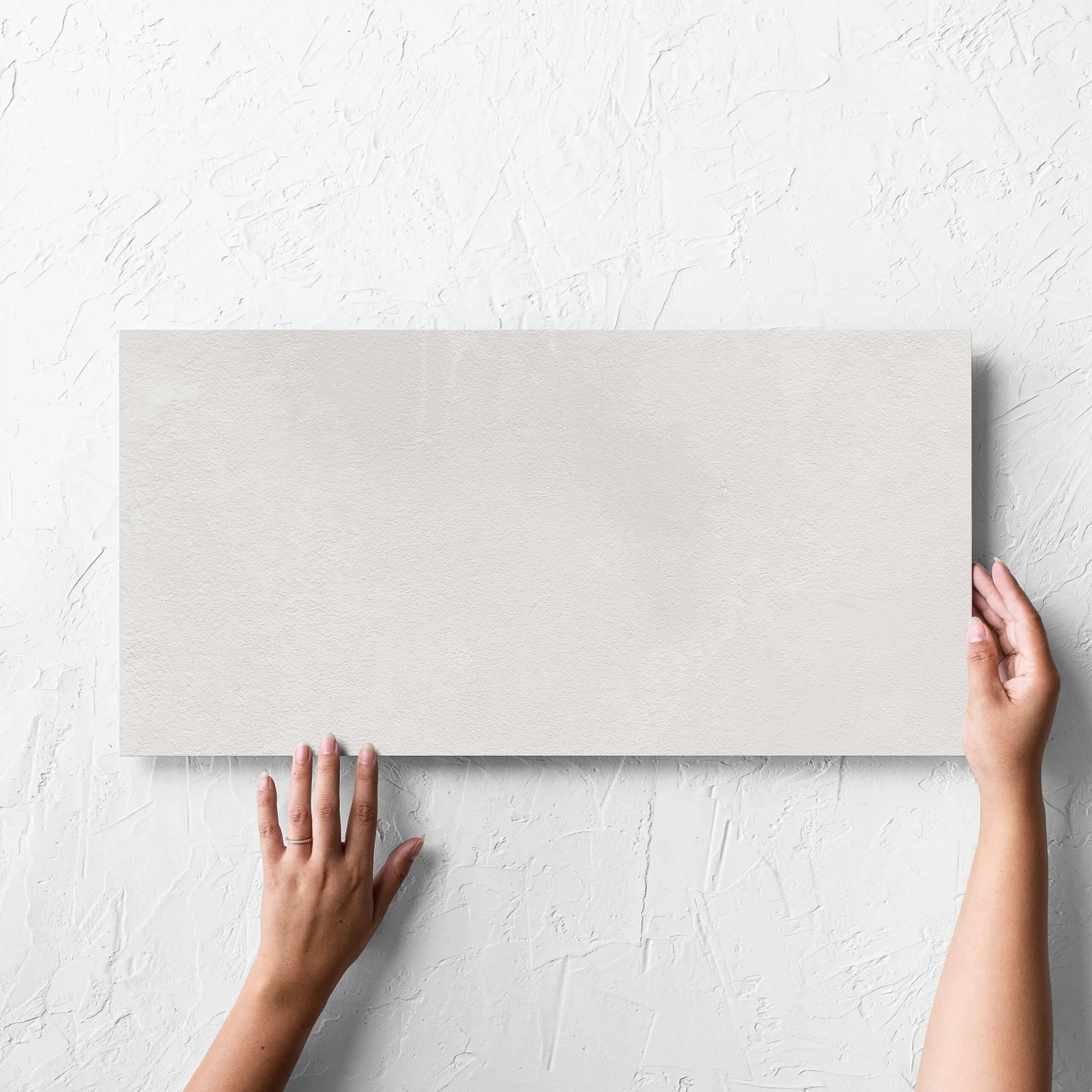 Hand holding a single Clay Bari White 300x600mm tile against a white rendered wall, showing the matt surface