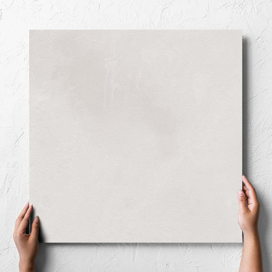 Hand holding a single Clay Bari White 600x600mm tile against a white rendered wall, showing the matt surface