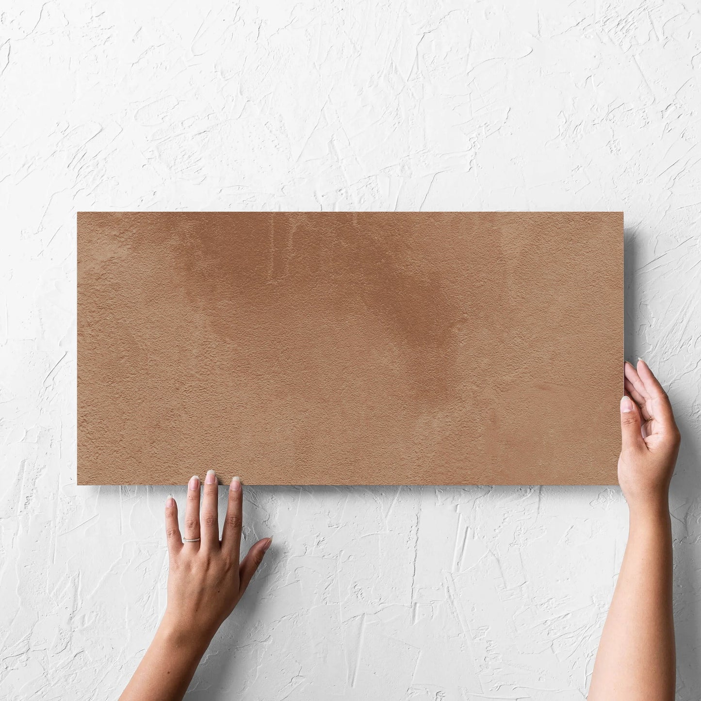 Hand holding a single Clay Firenze Dark Terracotta 300x600mm tile against a white rendered wall, showing the matt surface