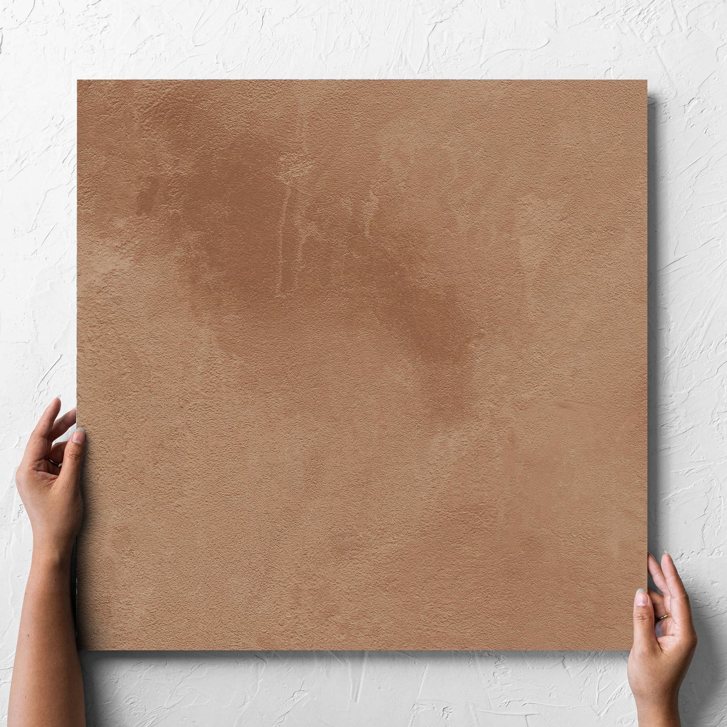 Hand holding a single Clay Firenze Dark Terracotta 600x600mm tile against a white rendered wall, showing the matt surface
