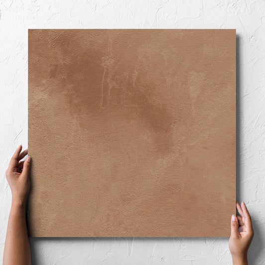 Hand holding a single Clay Firenze Dark Terracotta 600x600mm tile against a white rendered wall, showing the matt surface