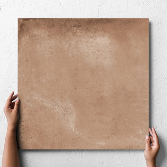 Hand holding a single Clay Orvieto Light Terracotta 600x600mm tile against a white rendered wall, showing the matt surface