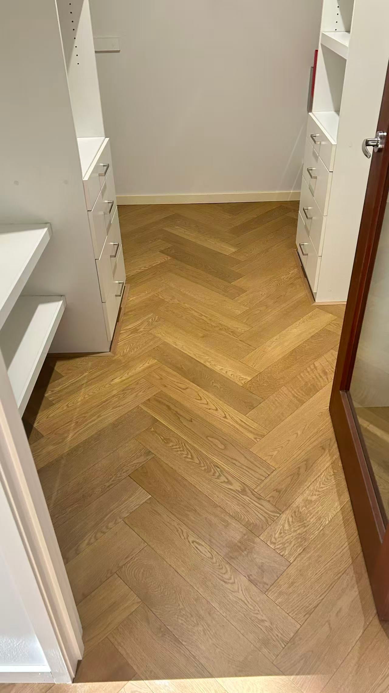 Coral Sand iDesign Herringbone Flooring 15/3mm installed in a walk-in wardrobe with white cabinetry and drawers, showcasing a warm oak chevron pattern.