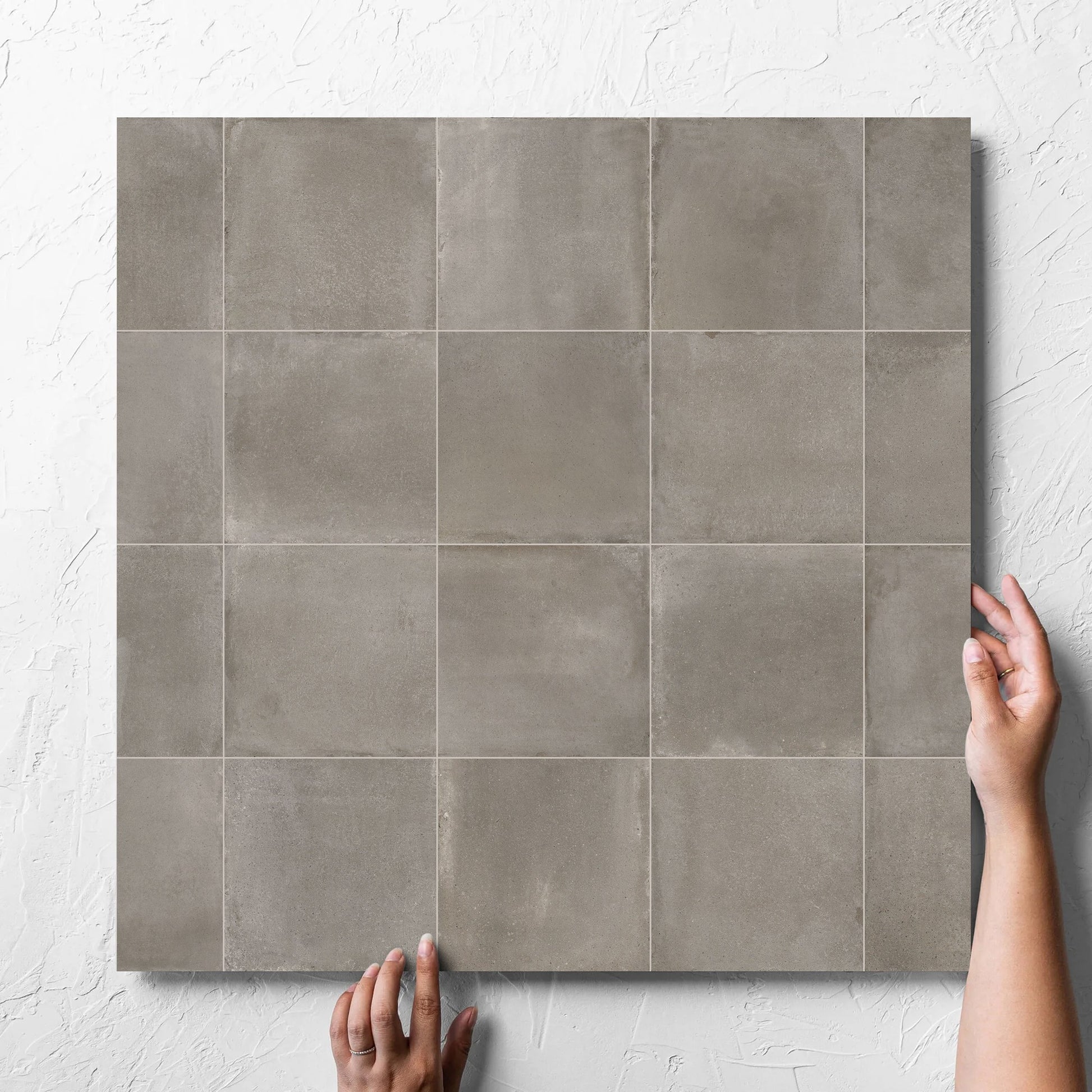 Hand holding a single Cotto Concrete Matt 600x600mm tile against a white rendered wall, showing the matt surface