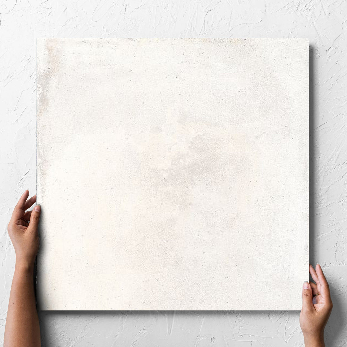Hand holding a single Cotto Ice Matt 600x600mm tile against a white rendered wall, showing the matt surface