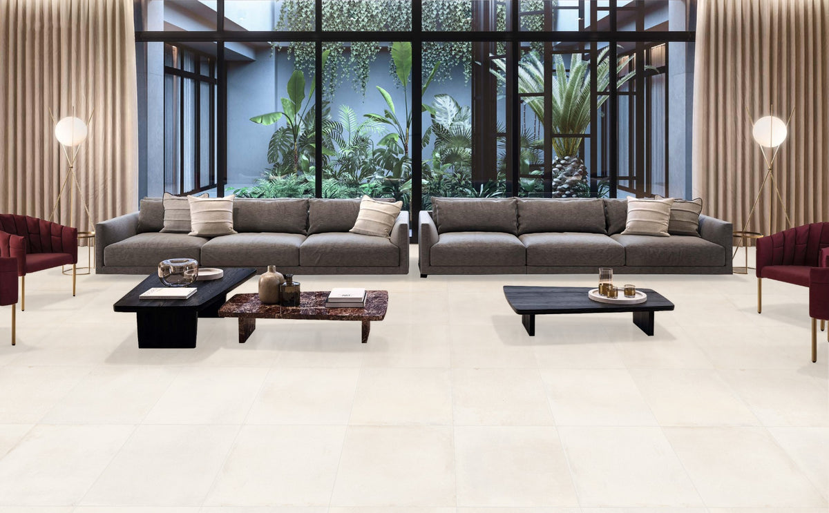 Cotto Ice Matt 600x600mm floor tiles in a luxury living room with grey sofas, dark coffee tables, and floor-to-ceiling windows overlooking tropical greenery.