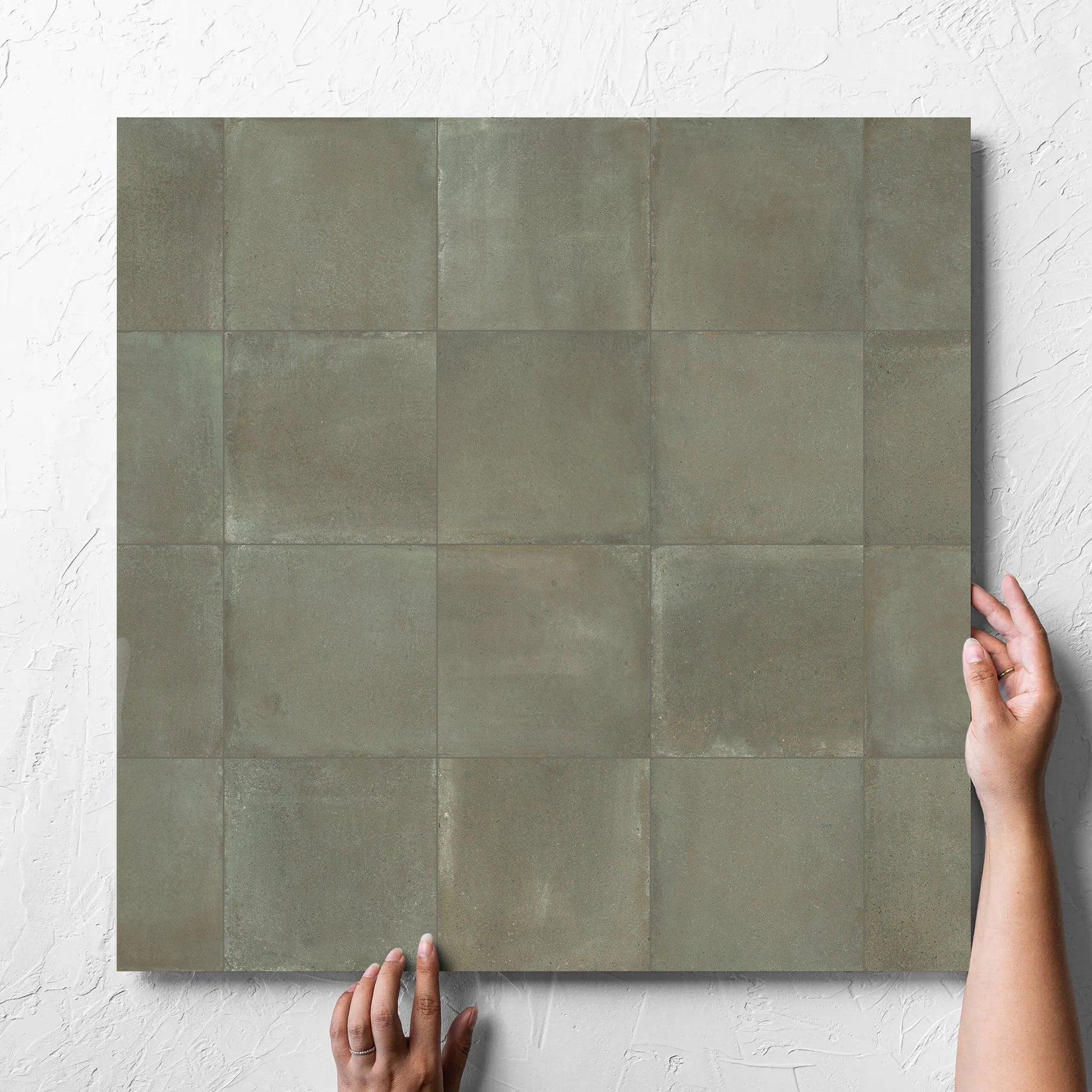 Hand holding a single Cotto Khaki Matt 600x600mm tile against a white rendered wall, showing the matt surface